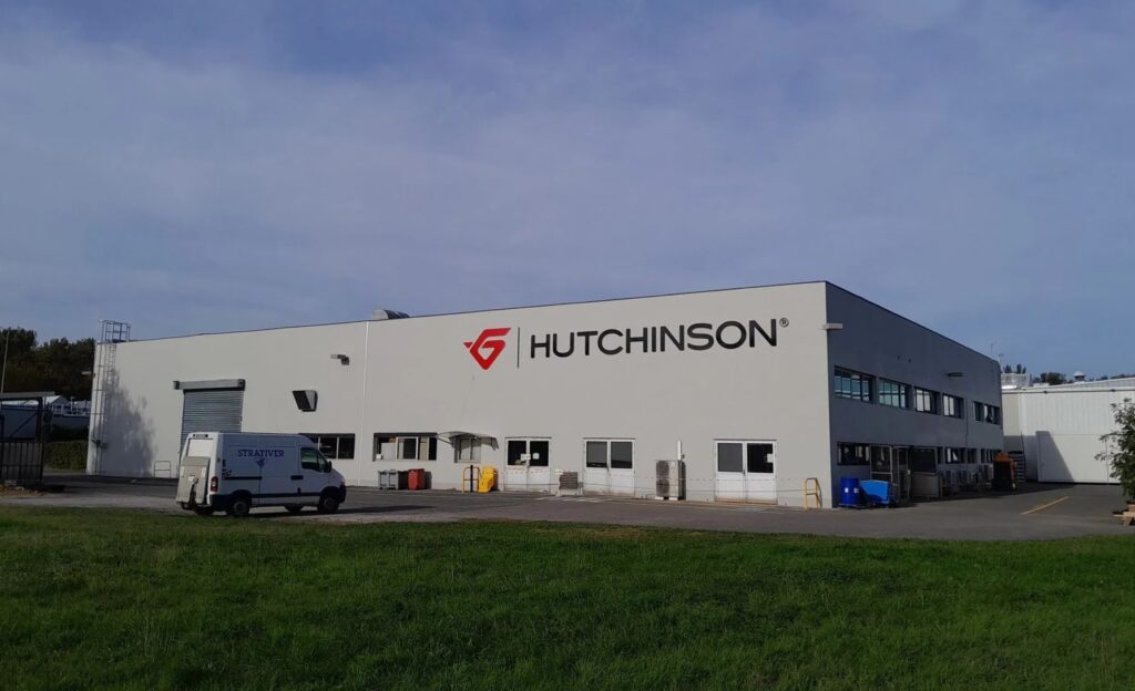 Enseigne de site industriel grand format pour l'entreprise Hutchinson réalisée par Becker Publicité. Exemple de signalétique extérieure monumentale et de marquage de façade pour un bâtiment d'usine ou logistique.
